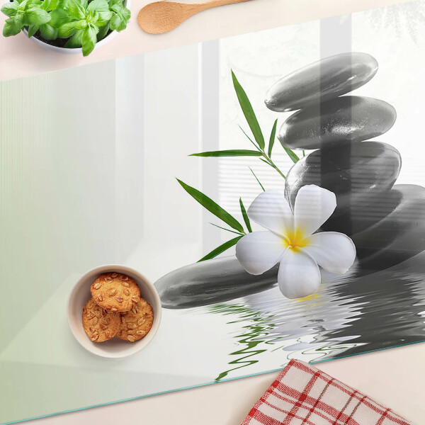 Schneidebrett mit Motiv aus Blumen und Kieselsteinen auf Wasser