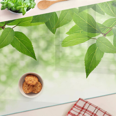 Glas-Schneidebrett mit Blattmotiv vor verschwommenem grünen Hintergrund