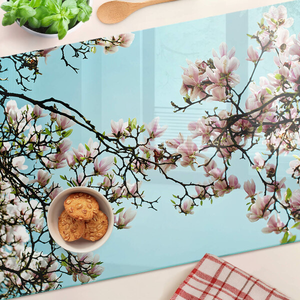 Glas-Schneidebrett mit Magnolienblüten auf blauem Hintergrund