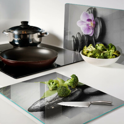 Schneidebrett Glas mit Steinen und Orchideen im Hintergrund