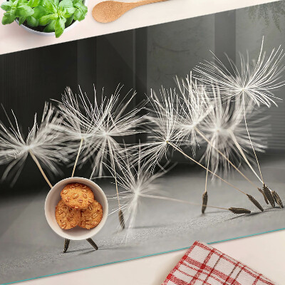 Glas Schneidebrett mit flauschigen Löwenzahnblüten auf einfarbigem Hintergrund