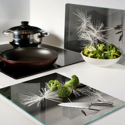 Glas Schneidebrett mit flauschigen Löwenzahnblüten auf einfarbigem Hintergrund