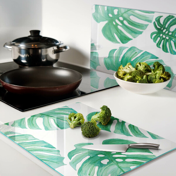 Glas-Schneidebrett mit Monstera-Blättern auf weißem Hintergrund