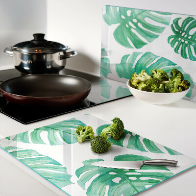 Glas-Schneidebrett mit Monstera-Blättern auf weißem Hintergrund