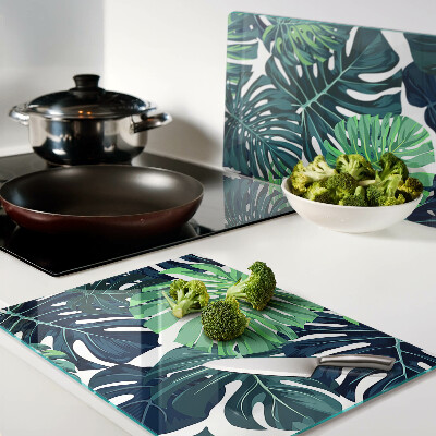 Schneidebrett Glas mit Monstera-Blättern vor tropischem Hintergrund