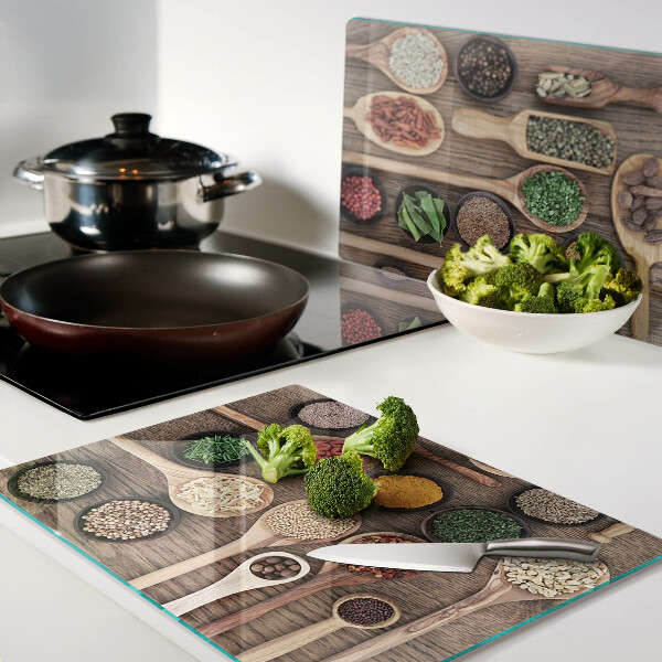 Glas-Schneidebrett mit Motiv aus Gewürzen und Kräutern in Holzlöffeln