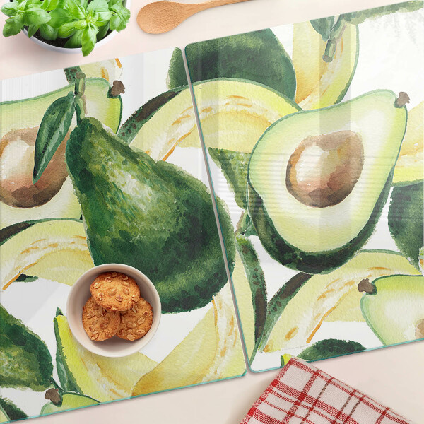 Glas-Schneidebrett mit Avocado-Motiv und Blättern im Hintergrund